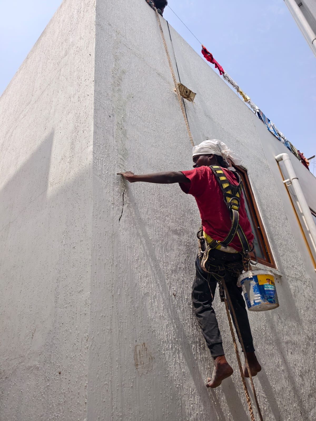 LoklFix technician applying waterproofing on exterior wall using rope access